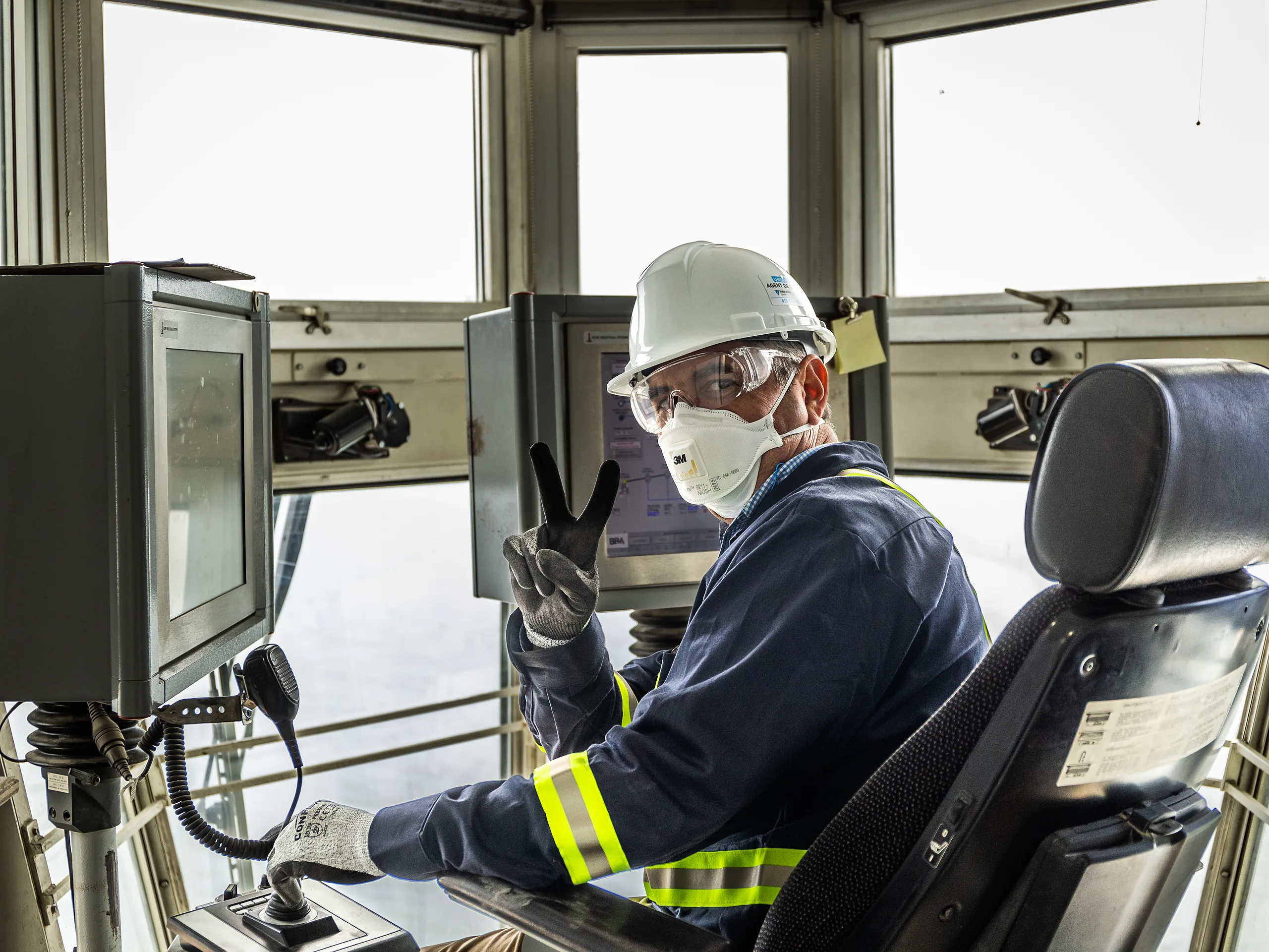 Building Materials Supplier - operator in a hard hat and mask at the controls of an equipment cab