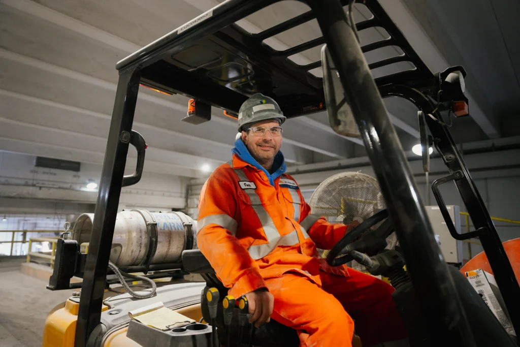 Seven Pillars of Sustainability - worker in orange coveralls and a hard hat driving a forklift in a warehouse