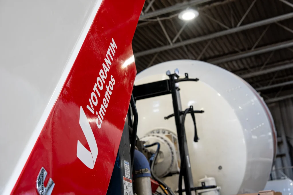 Cement and Concrete Solutions - Votorantim Cimentos branding on a red truck panel beside a mixer drum in a fleet garage