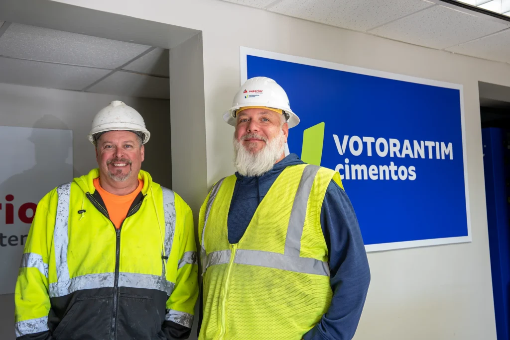 Cement and Concrete Solutions - two workers in hard hats and safety vests in front of a Votorantim Cimentos sign